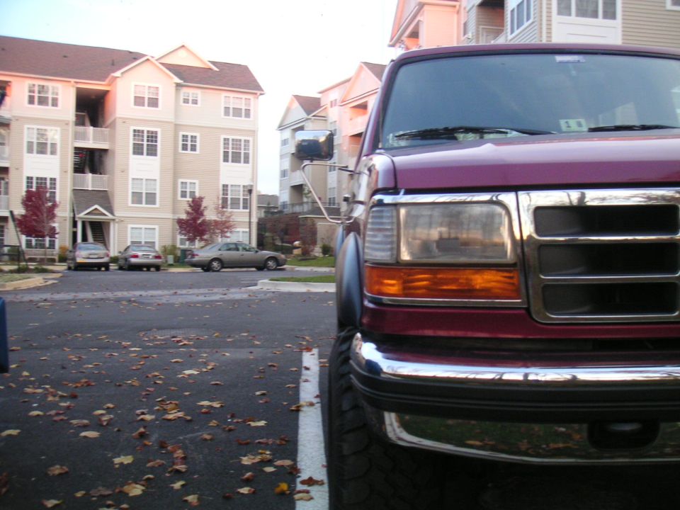Maroon Ford truck front grille and headlight, parked in apartment complex lot