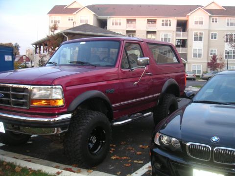 1994 Ford Bronco - A lifted red 1994 Ford Bronco is parked in a lot next to a black BMW.