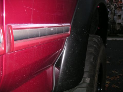 1994 Ford Bronco - Close-up of the red rear quarter panel and lower body-side molding on a lifted SUV, showing the black textured fender flare meeting the she…