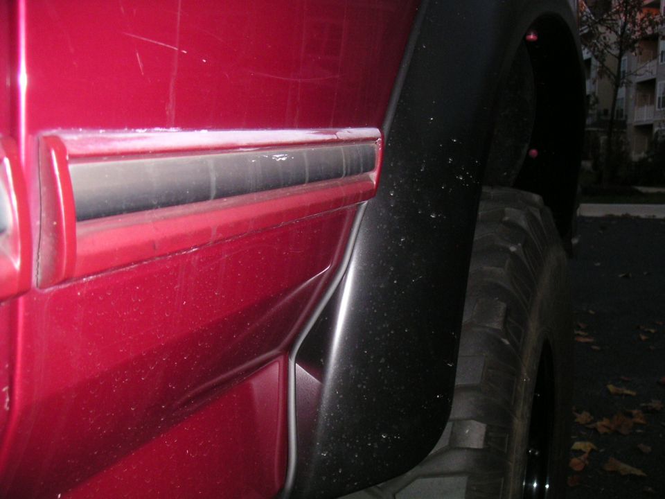 Red SUV rear quarter with black fender flare, chrome body molding and mud-terrain tire