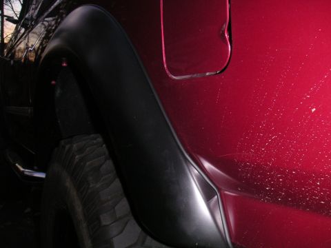 1994 Ford Bronco - Night close-up of a red truck's rear quarter panel with a black bolt-on fender flare over an aggressive mud-terrain tire, showing the chrom…