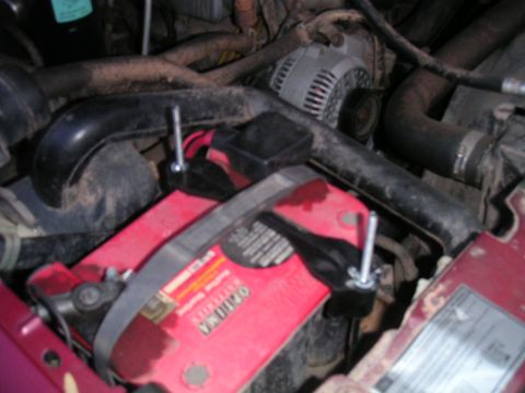 1994 Ford Bronco - The engine bay shows a red Optima battery secured with metal brackets and bolts, surrounded by hoses and an alternator.