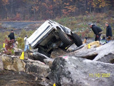 1995 Ford Bronco - A white 1995 Ford Bronco is overturned on a rocky terrain, with spectators observing the scene.
