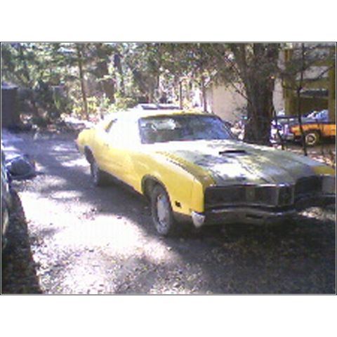 1971 Mercury Cyclone - A yellow muscle car with black hood stripes is parked on a gravel driveway under trees.