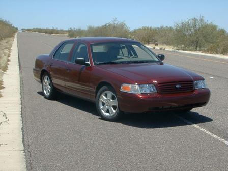 2004 Ford Crown Victoria - A maroon 2004 Ford Crown Victoria sedan is parked on the side of a desert highway.