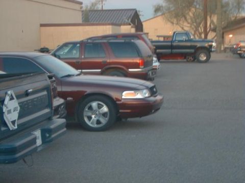 2004 Ford Crown Victoria - Multiple vehicles parked in a lot, including a maroon Ford Crown Victoria and a dark pickup truck.