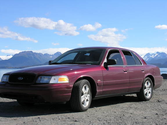Maroon Ford sedan parked on gravel with mountains and water behind.