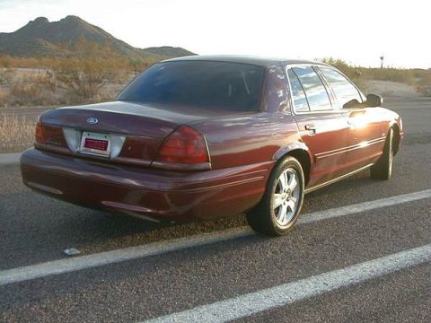 2004 Ford Crown Victoria - A maroon sedan is parked on the side of a desert road, viewed from the rear quarter angle.