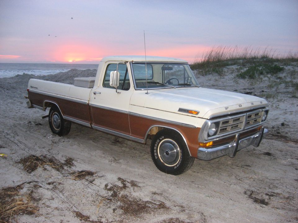 1972 Ford F-100 pickup truck with woodgrain trim parked on a beach at sunset