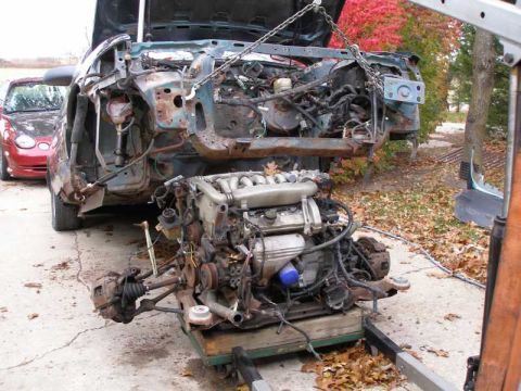 1993 Ford Taurus - Engine removed from a car and placed on a stand, with another vehicle visible in the background.