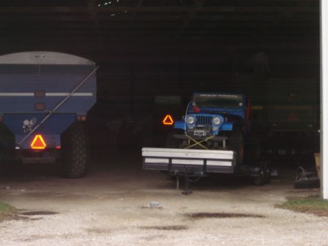 1992 Ford Bronco - A blue Jeep is parked on a trailer inside a barn, with a large grain cart to its left.