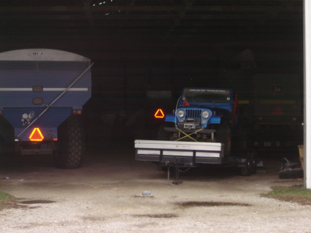 Blue Jeep on a trailer inside a barn, next to a large blue grain cart