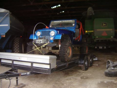 1992 Ford Bronco - A blue Jeep Wrangler is loaded onto a trailer inside a barn.