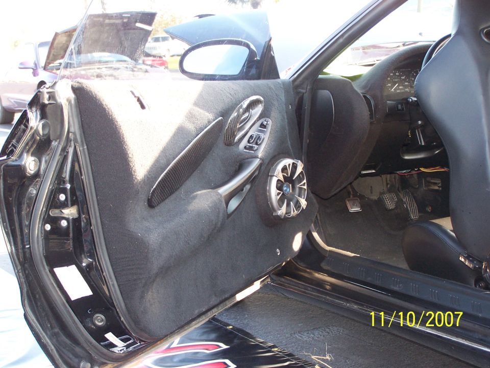 Car interior door panel with aftermarket speaker and carbon fiber trim, driver's side