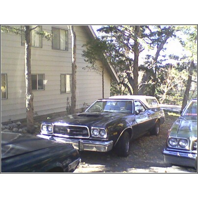 1973 Ford Ranchero - A black 1973 Ford Ranchero with a white camper shell is parked next to another vehicle.
