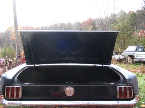 1966 Ford Mustang - The rear of a 1966 Ford Mustang shows its open trunk and iconic badge, with a pickup truck visible in the background.
