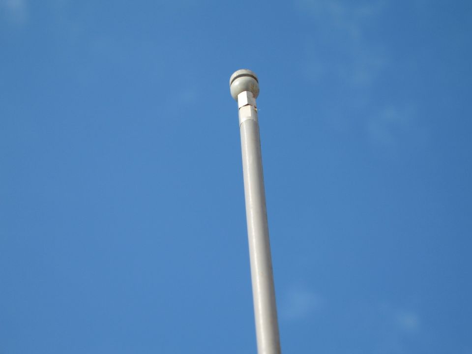 Flagpole against a blue sky with a Supermotors logo at the bottom right