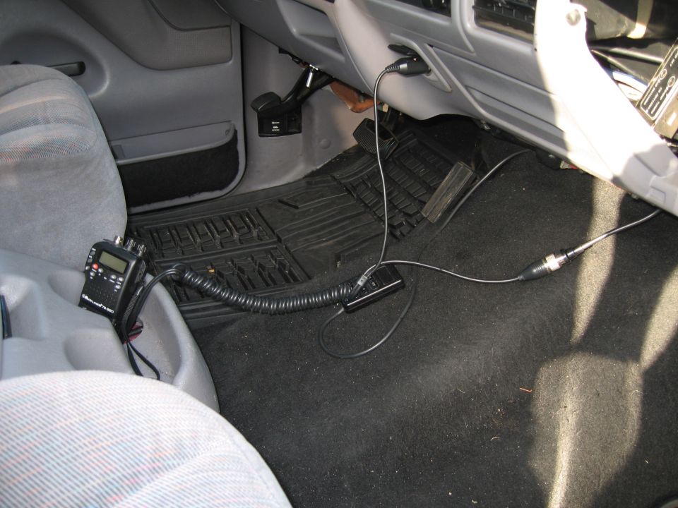 Interior shot of a vehicle's passenger side floor and dashboard, showing a CB radio mounted on the center console and its wiring