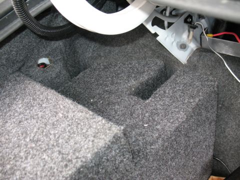 1997 Ford Crown Victoria - The carpeted interior of a car's trunk shows some exposed wiring and metal brackets.