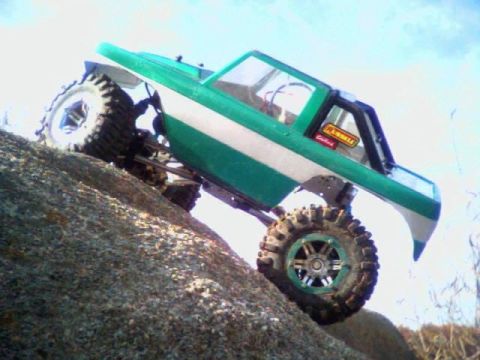 1996 Ford Bronco - RC rock crawler navigates a rocky incline under a bright sky.