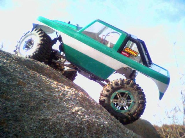 Green and white RC rock crawler on a rock, side view