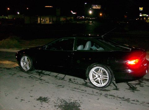 1995 Ford Probe - A black coupe with aftermarket wheels is parked on a wet surface at night.
