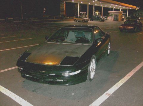1995 Ford Probe - A dark-colored Ford Probe is parked at a gas station, with other vehicles in the background under the station lights.