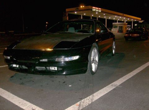 1995 Ford Probe - A black coupe is parked at a gas station, with another vehicle visible in the background.