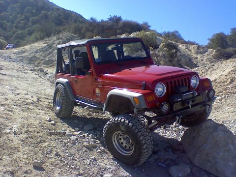 1994 Ford Bronco - A red Jeep Wrangler navigates a rocky off-road trail under a clear blue sky.