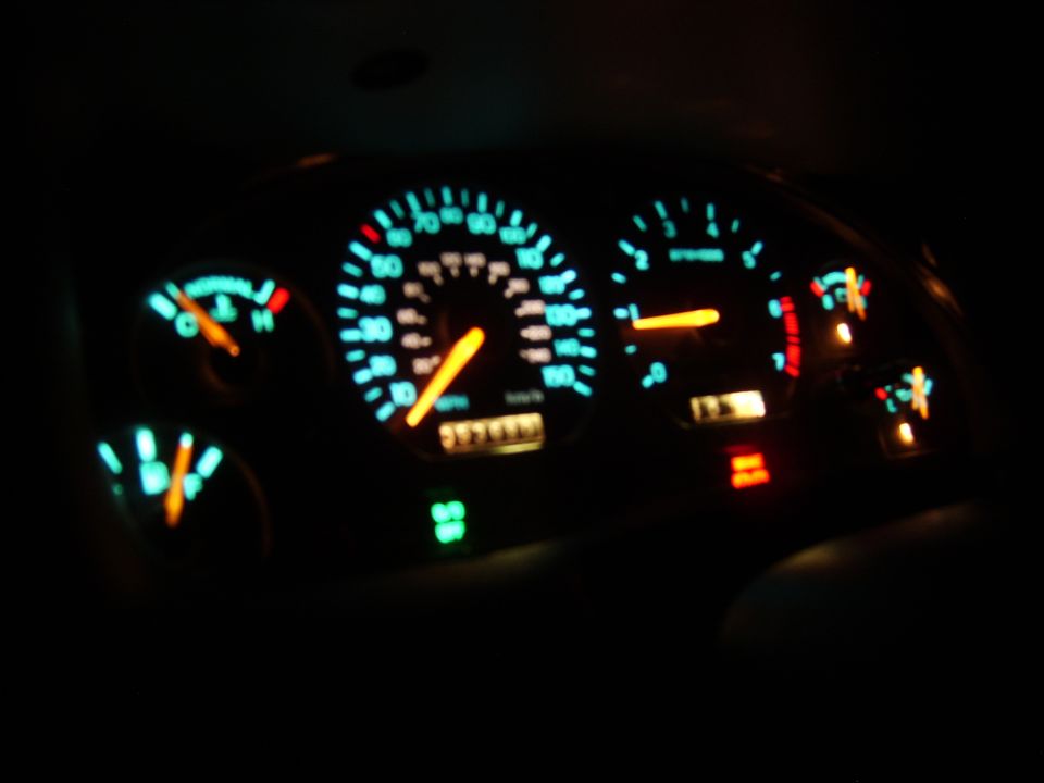 Illuminated car gauge cluster at night with teal backlight and orange needles