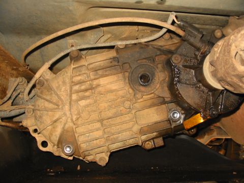1988 Ford Bronco - Underside view of a vehicle's transfer case and driveshaft, showing signs of wear and fluid leakage.