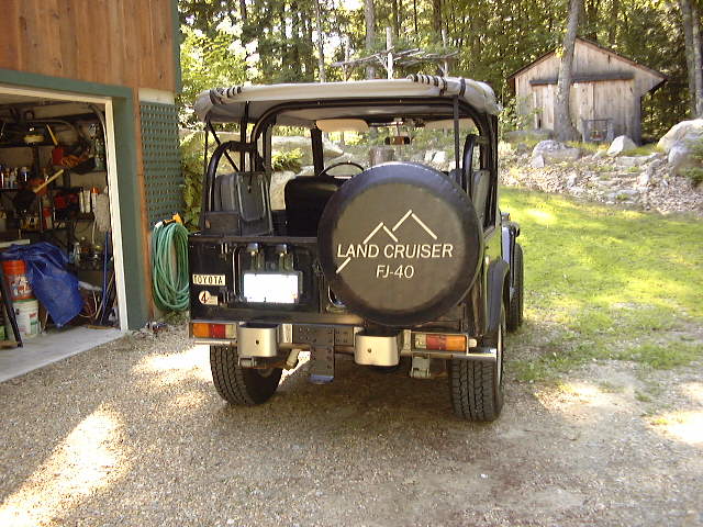 Rear view of a 1974 Toyota Land Cruiser FJ40 parked in a gravel driveway next to a garage
