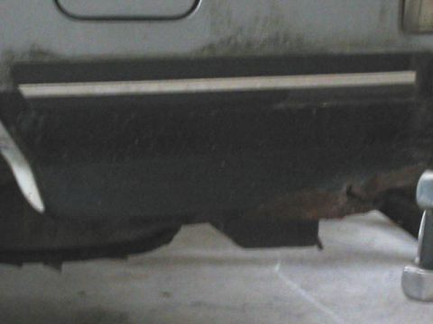 1989 Ford Bronco - The lower body panel of a vehicle shows significant rust and damage.
