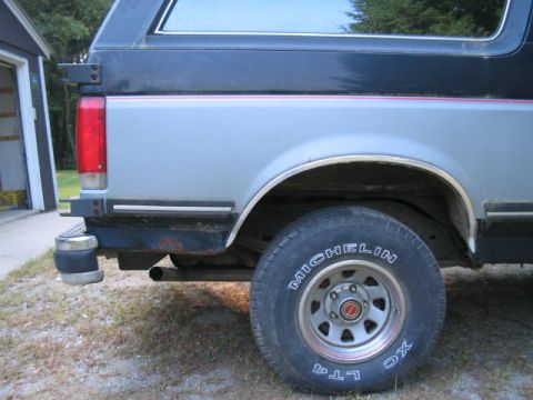 1989 Ford Bronco - The rear of a two-tone Ford Bronco is visible, with a garage in the background.