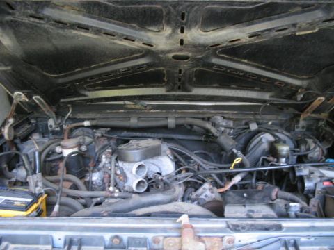 1989 Ford Bronco - View of the engine compartment, including the V8 engine, battery, and various hoses and wires.