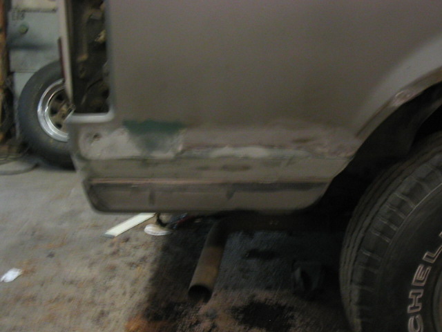 Rear quarter panel of a vehicle undergoing body repair, showing primer and body filler