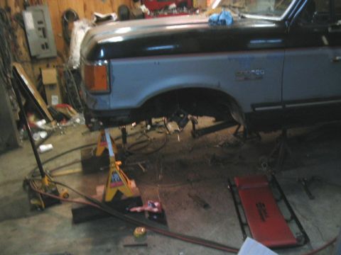 1989 Ford Bronco - 1989 Ford Bronco undergoing lift installation, showing the side profile while supported by jack stands.