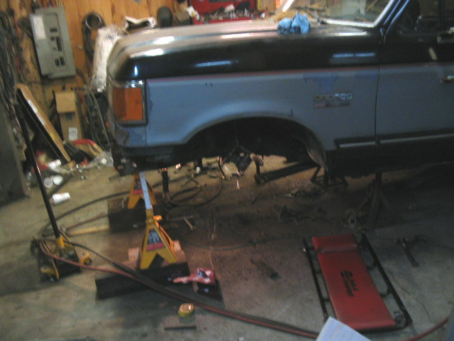 1989 Ford Bronco side view, lifted on jack stands in a garage with suspension components visible