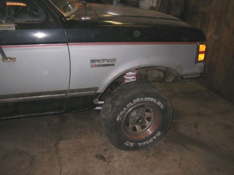 1989 Ford Bronco - A two-tone Ford Bronco is shown with its front wheel and suspension components visible.