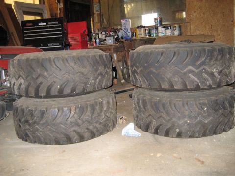 1995 Ford Bronco - Four off-road tires are stacked in a garage, with tools and supplies visible in the background.