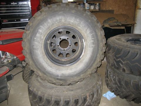 1995 Ford Bronco - A set of large tires and rims are stacked in a garage, with a red lawn tractor visible in the background.