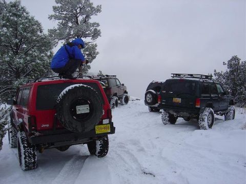 1956 Ford Bronco II - Multiple Jeep Cherokees navigate a snowy trail, with one vehicle prominently a spare tire mounted on its rear.