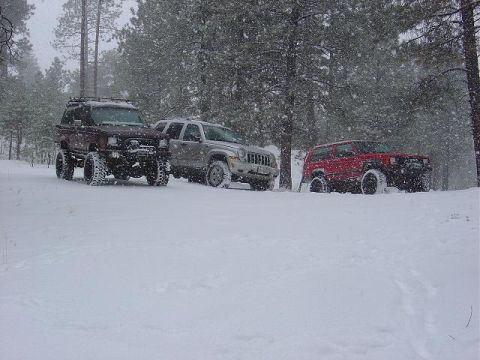 1956 Ford Bronco II - Three SUVs are parked in a snowy forest as snow falls around them.