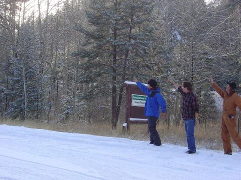 1956 Ford Bronco II - Three men gesture towards a sign in a winter forest scene, possibly indicating a location or point of interest.