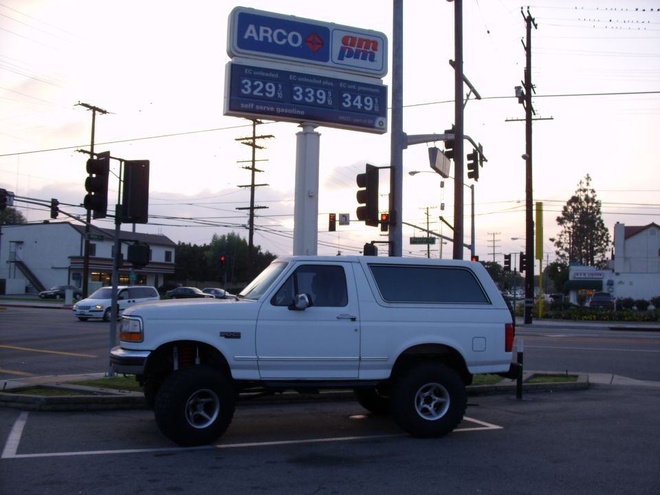 Lifted white Ford Bronco SUV in side view parked under an ARCO am/pm gas price sign at dusk