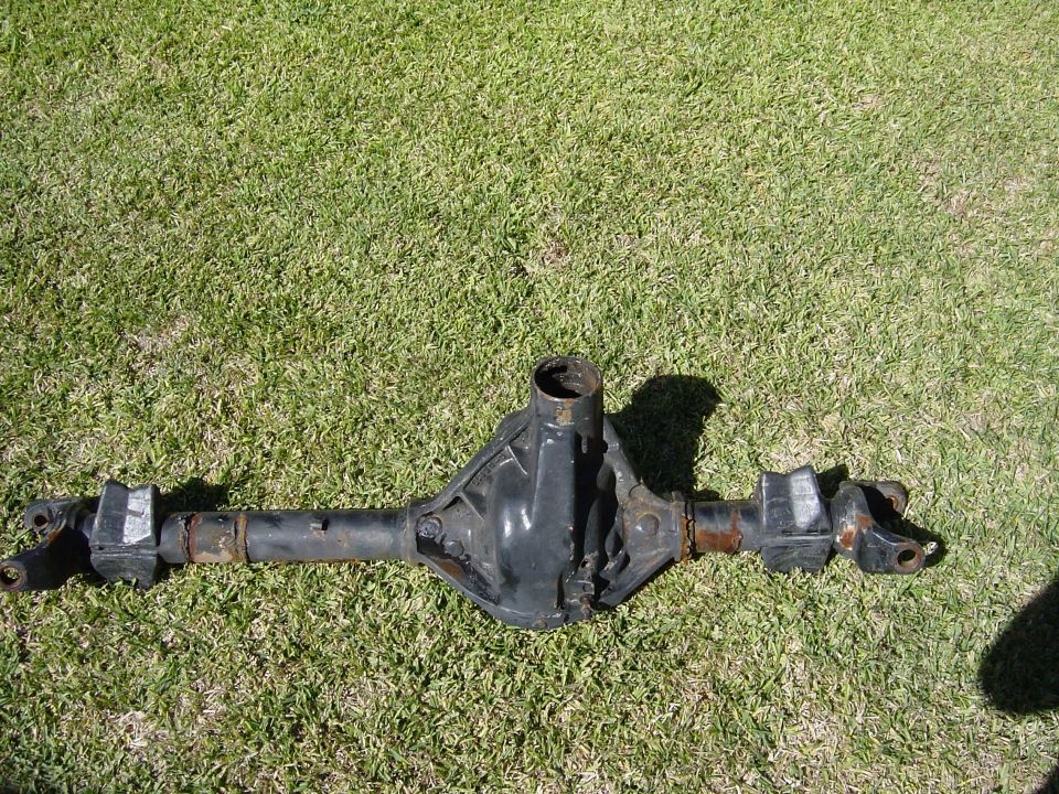 Stripped solid front axle housing with spring perches lying on grass