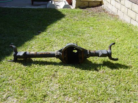1983 Ferrari Enzo - A rusty rear axle differential housing sits on a grassy lawn in front of a brick wall.
