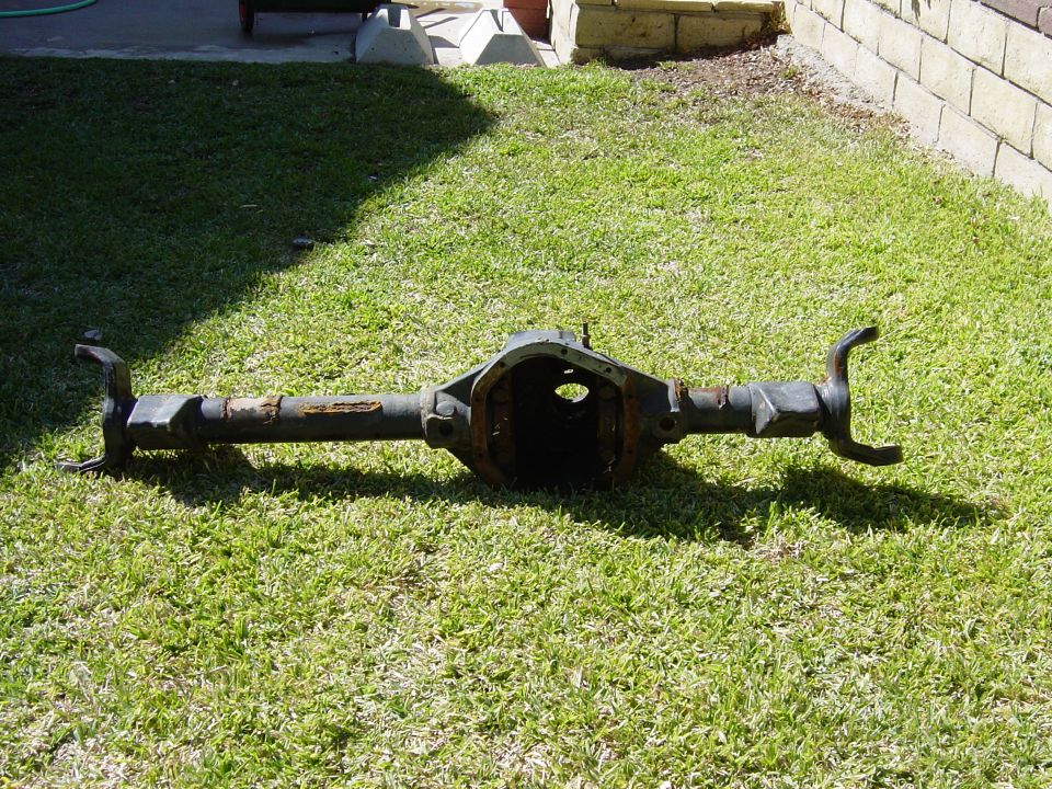 Stripped rear axle housing with empty differential opening lying on grass