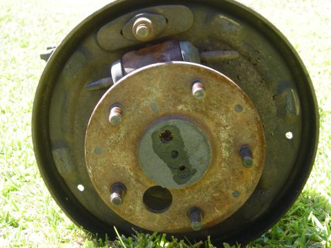 1983 Ferrari Enzo - A close-up view of a rusty brake drum assembly, showing the hub and wheel studs against a grassy background.