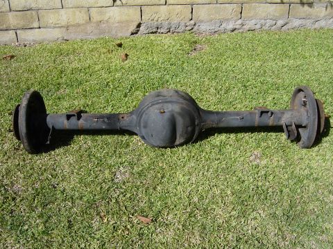 1983 Ferrari Enzo - A rear axle assembly with brake drums sits on a grassy lawn in front of a brick wall.